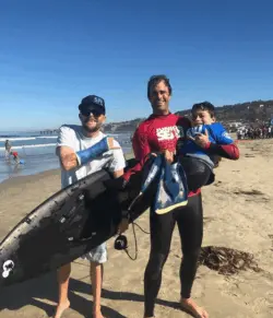 Ryan Eick, a man, and child posing at the beach with a surfboard