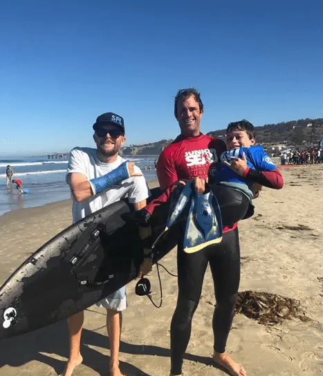 Ryan Eick, a man, and child posing at the beach with a surfboard